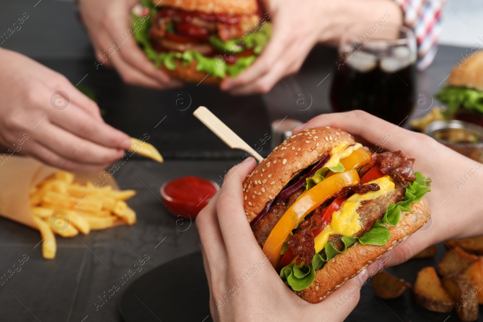 Photo of Woman with tasty burger and her friends at table, closeup