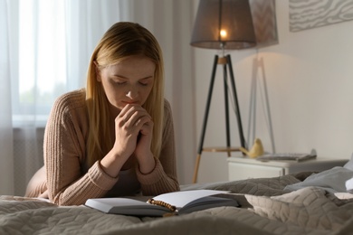 Photo of Religious young woman praying over Bible in bedroom