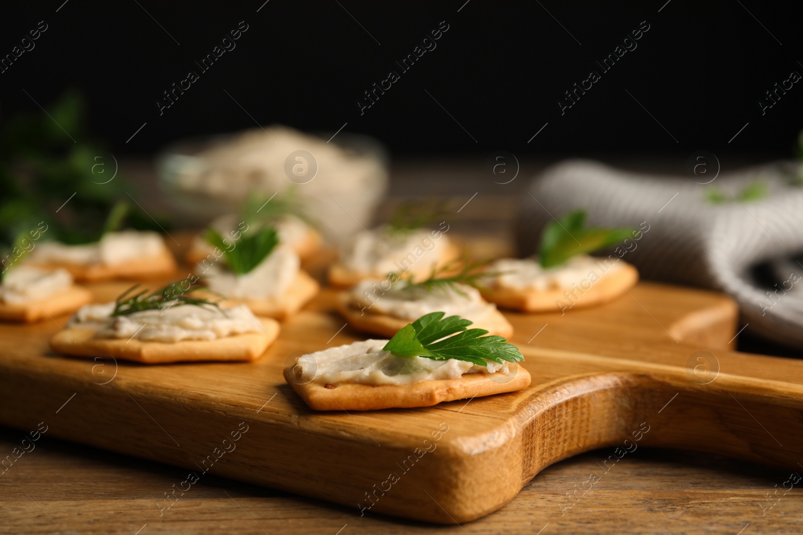 Photo of Delicious crackers with humus, parsley and dill on wooden table, closeup