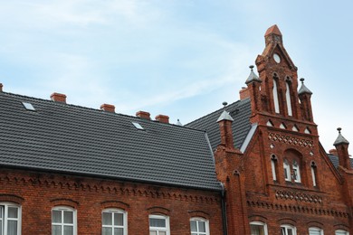 Photo of Beautiful red brick building with grey roof against blue sky, low angle view