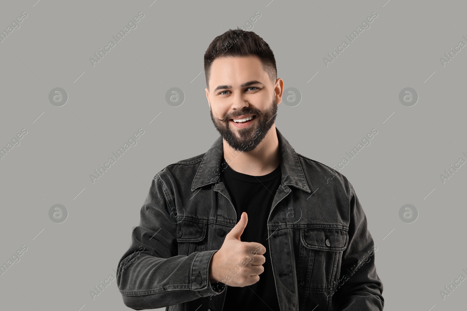 Photo of Portrait of bearded young man showing thumb up on grey background