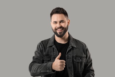 Portrait of bearded young man showing thumb up on grey background