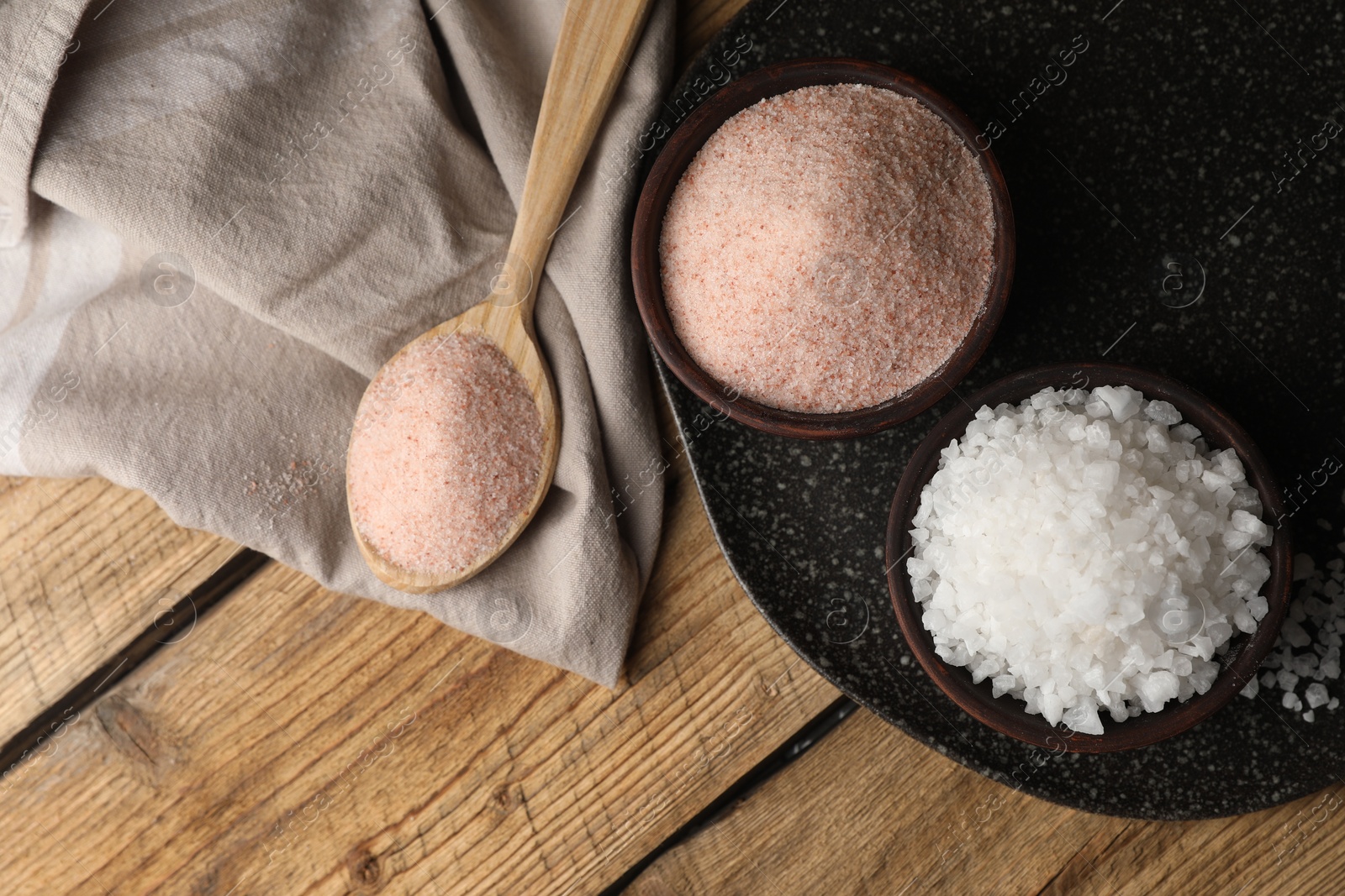 Photo of Different natural salt on wooden table, flat lay. Space for text