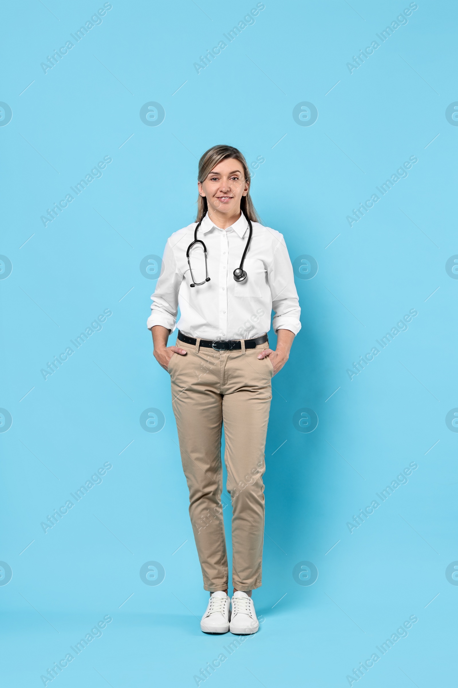 Photo of Portrait of happy doctor with stethoscope on light blue background