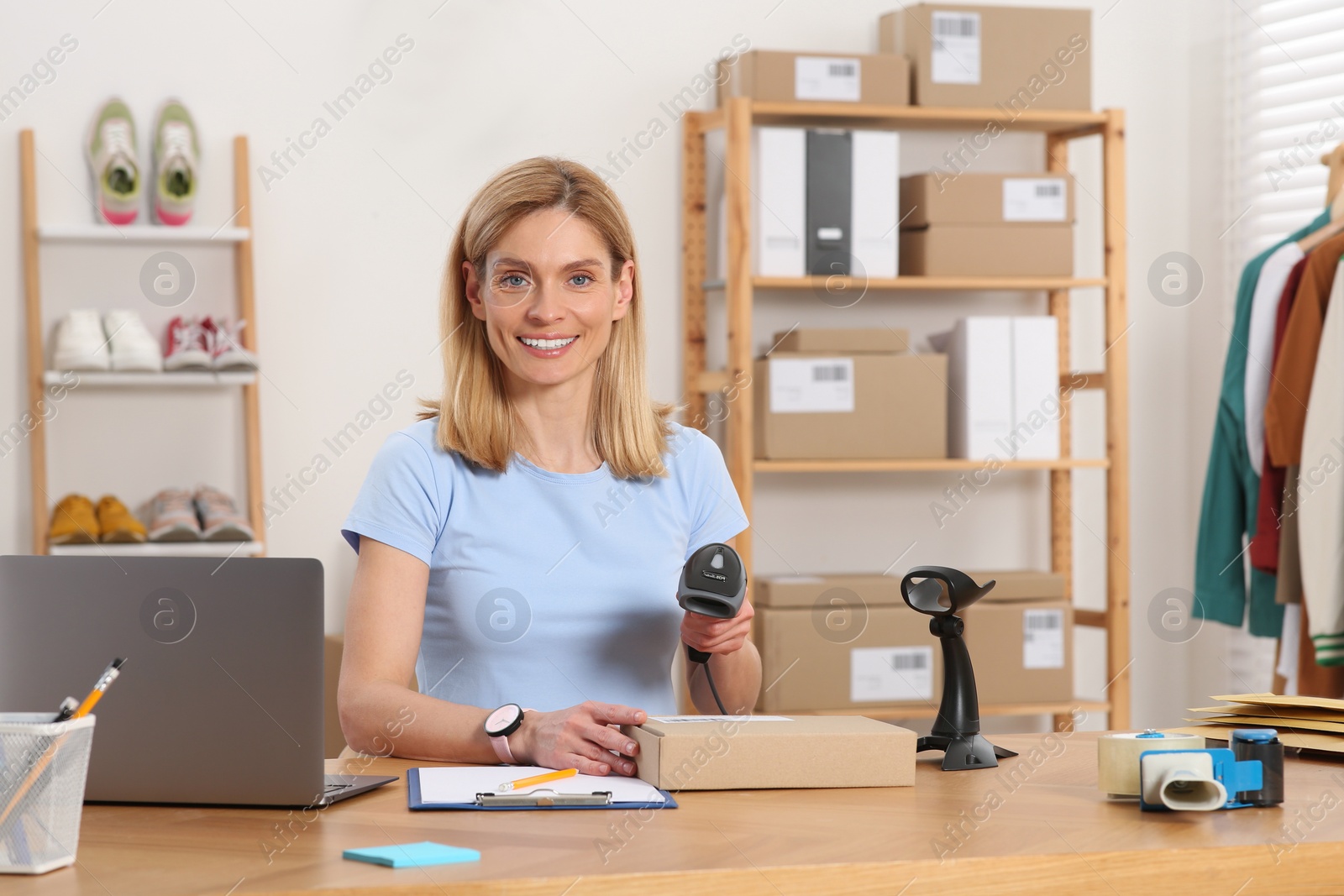 Photo of Seller with scanner reading parcel barcode at table in office. Online store