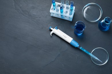 Photo of Laboratory analysis. Micropipette, petri dishes, beaker, flask and test tubes on black table, flat lay. Space for text