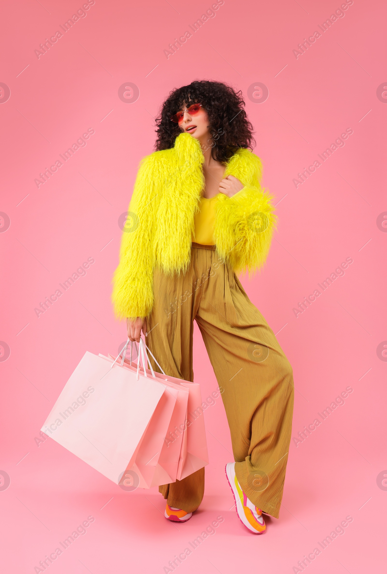 Photo of Happy young woman with shopping bags on pink background