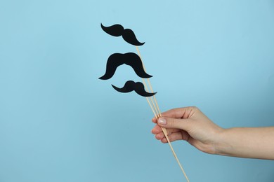 Photo of Woman with fake paper mustaches on light blue background, closeup. Space for text