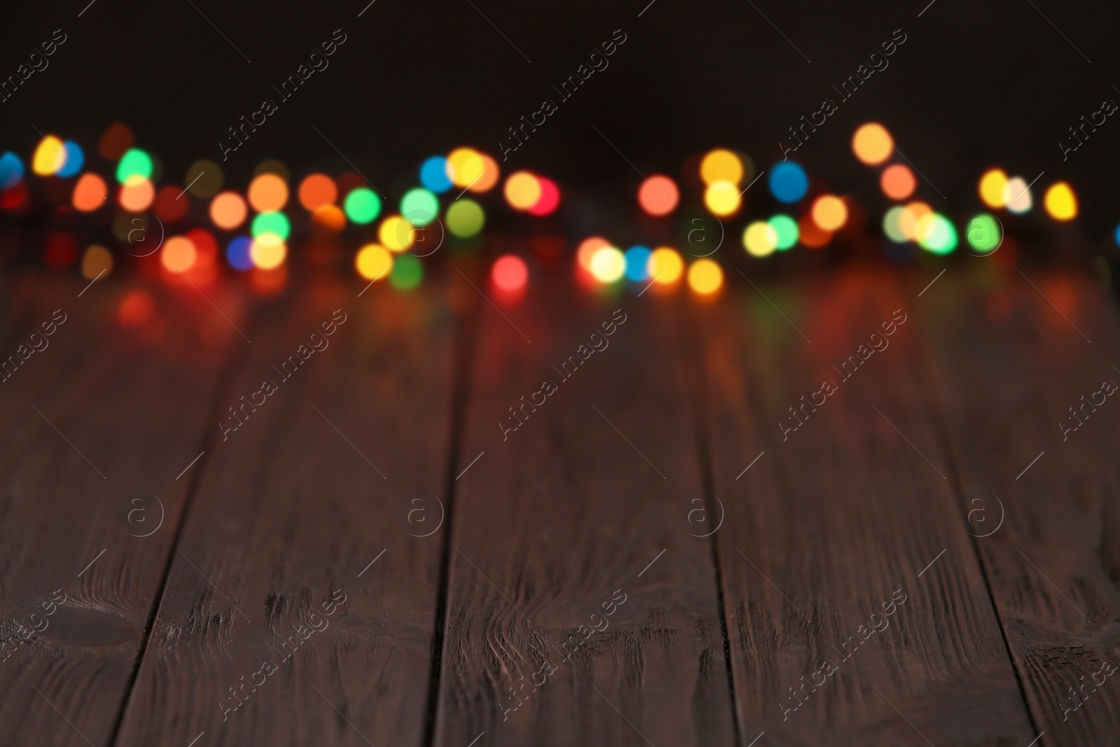 Photo of Colorful lights on wooden table, blurred view. Space for text
