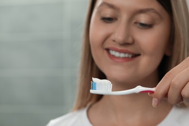 Young woman holding brush with toothpaste in bathroom, focus on hand. Space for text