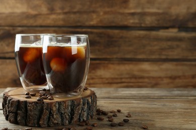 Glasses of delicious iced coffee served on wooden table, space for text