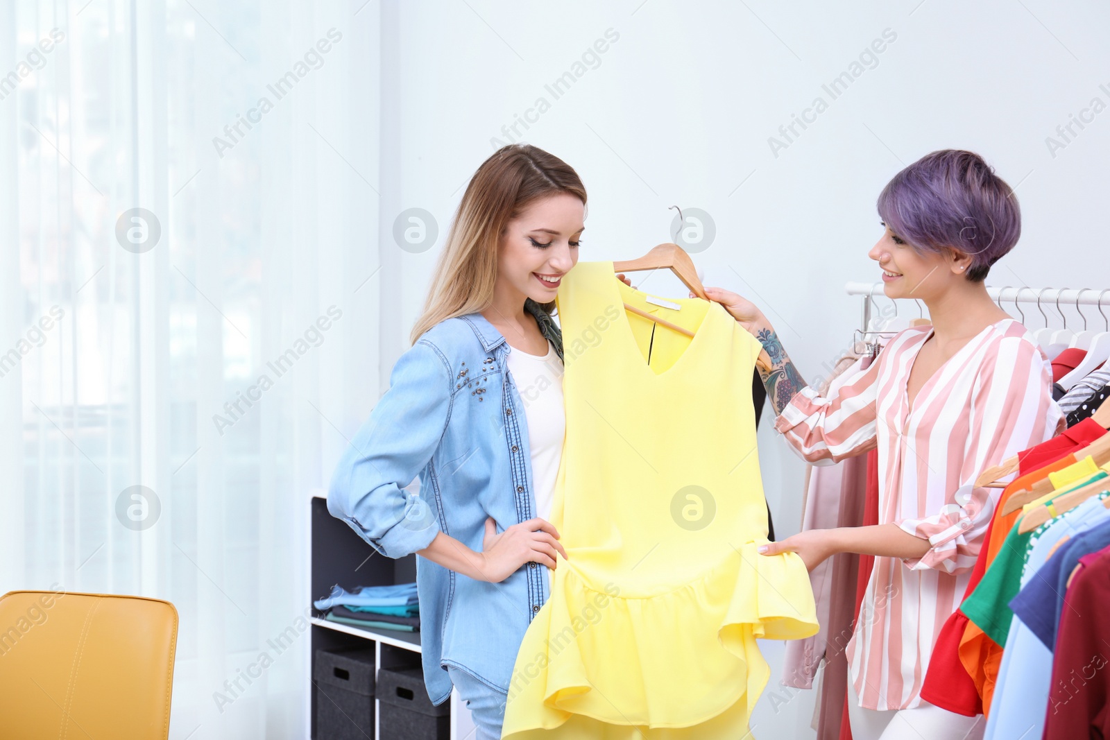 Photo of Young stylist helping customer to choose clothes indoors