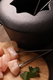 Fondue pot with oil, forks, raw meat pieces and parsley on wooden table, closeup
