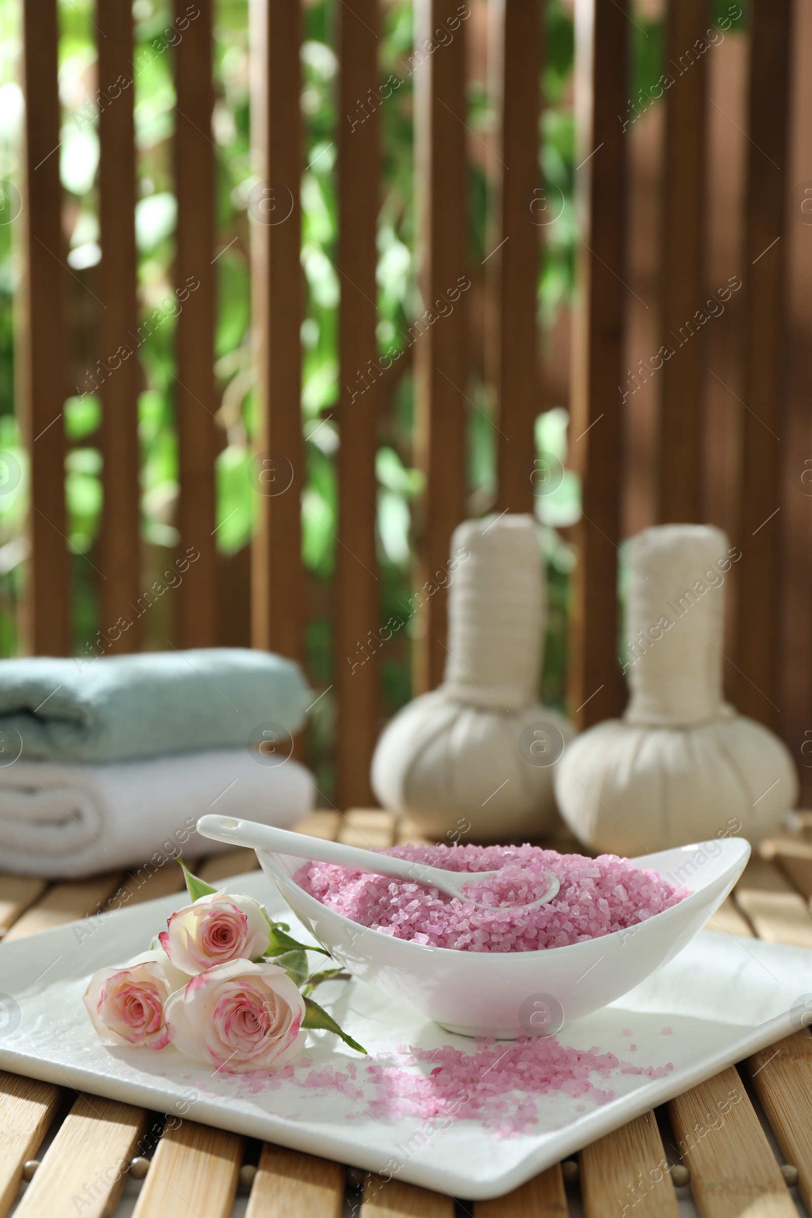 Photo of Bowl of pink sea salt and beautiful roses on wooden table, space for text