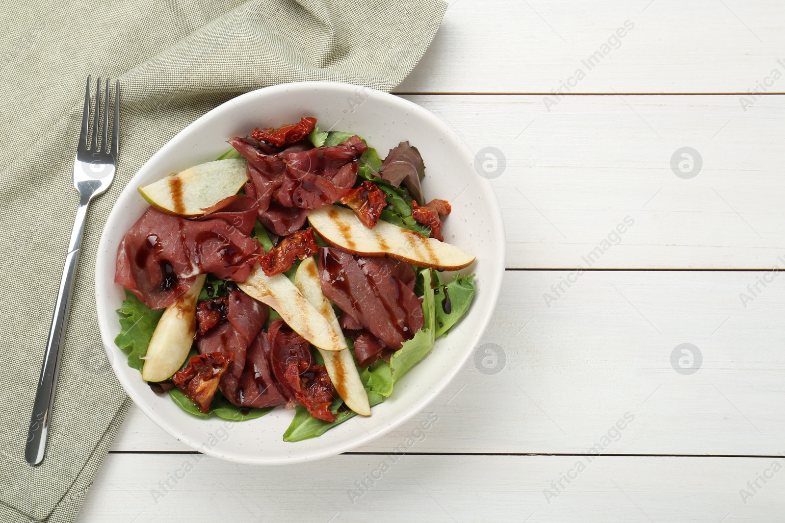 Photo of Delicious bresaola salad with sun-dried tomatoes, pear, balsamic vinegar and fork on white wooden table, flat lay. Space for text