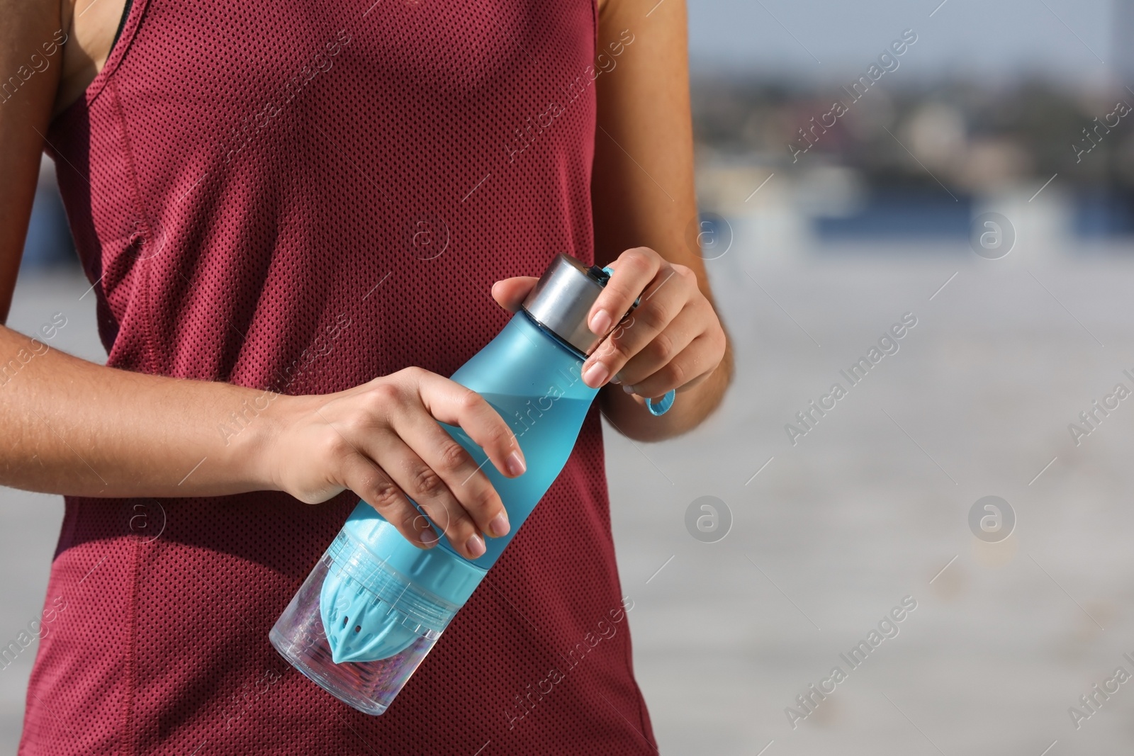 Photo of Sporty woman holding bottle of water outdoors on sunny day, closeup. Space for text