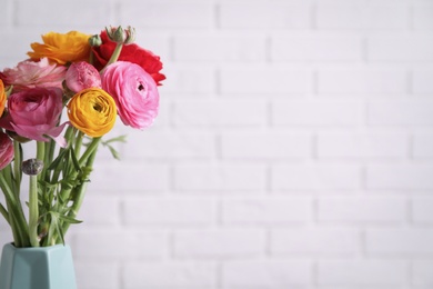 Photo of Beautiful fresh ranunculus flowers near white brick wall. Space for text