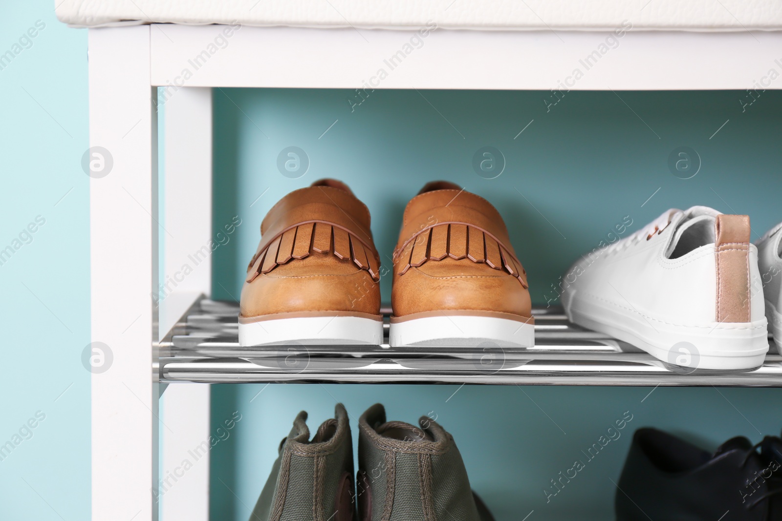 Photo of Collection of stylish shoes on rack storage near color wall