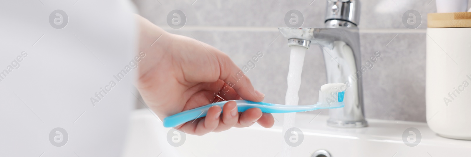 Image of Woman holding plastic toothbrush with paste above sink in bathroom, closeup. Banner design