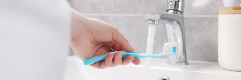 Woman holding plastic toothbrush with paste above sink in bathroom, closeup. Banner design