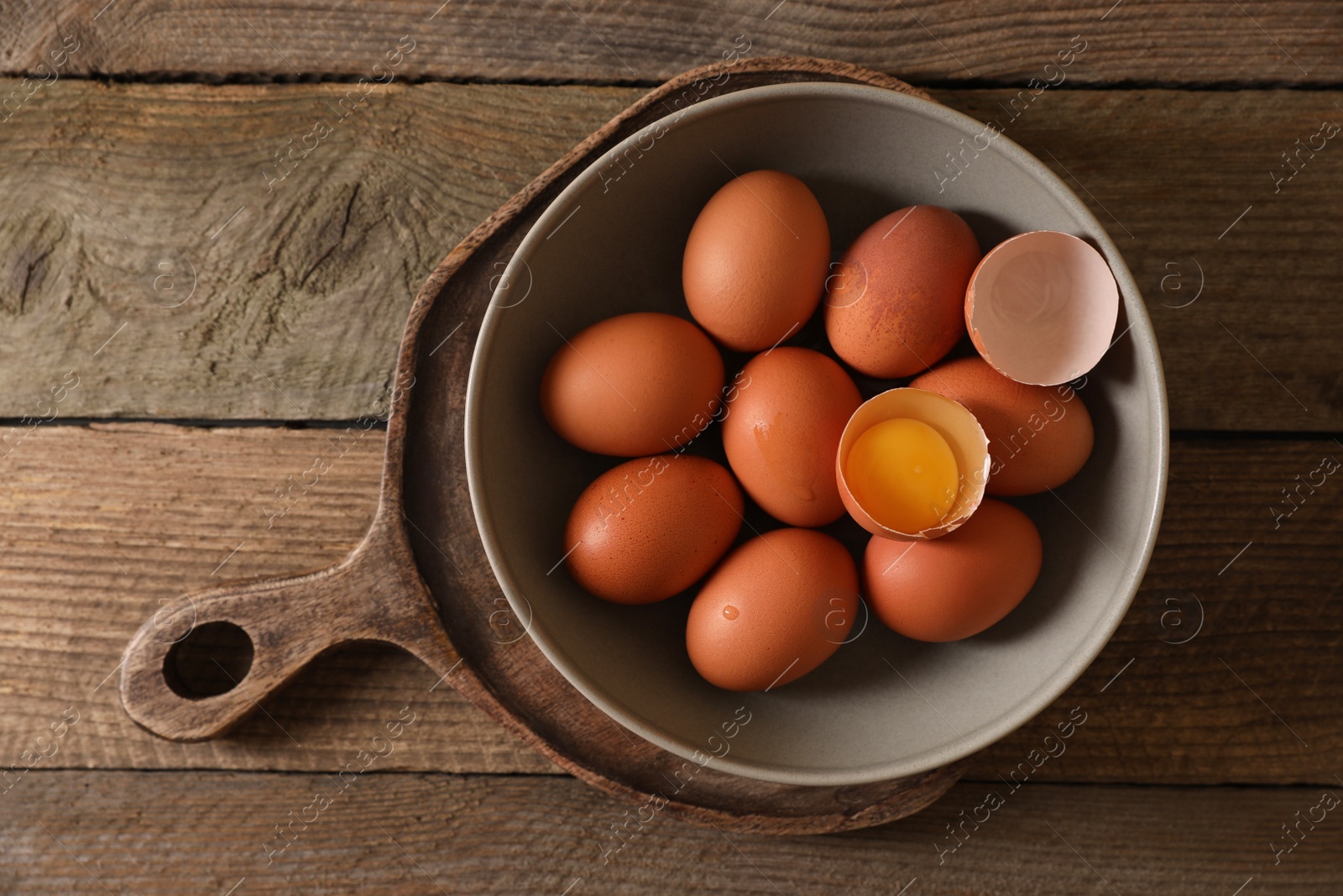 Photo of Bowl with raw chicken eggs on wooden table, top view