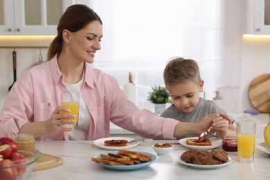 Photo of Mother and her cute little son having breakfast at table in kitchen