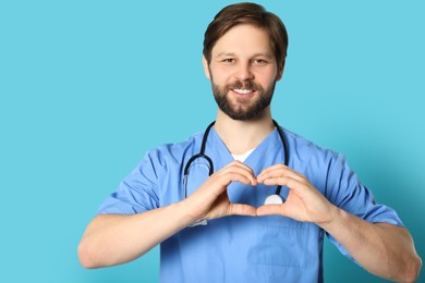Doctor or medical assistant (male nurse) making heart with hands on turquoise background