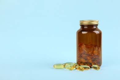 Jar with vitamin capsules on light blue background, space for text