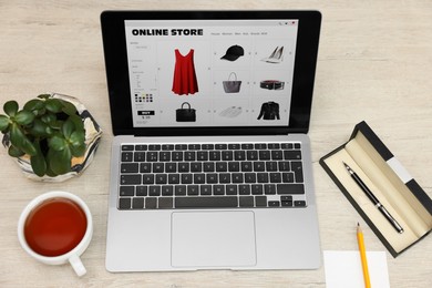 Photo of Online store. Laptop with open website, paper note, pen and pencil on wooden table, above view