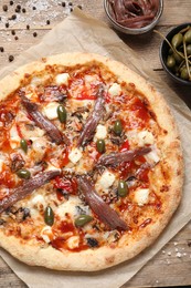 Photo of Tasty pizza with anchovies and ingredients on wooden table, flat lay