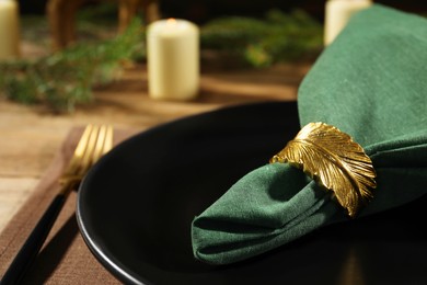 Photo of Green fabric napkin with beautiful decorative ring for table setting on black plate, closeup