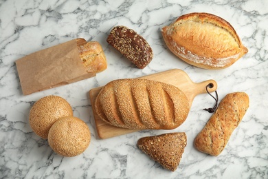 Photo of Different kinds of fresh bread on marble table, flat lay