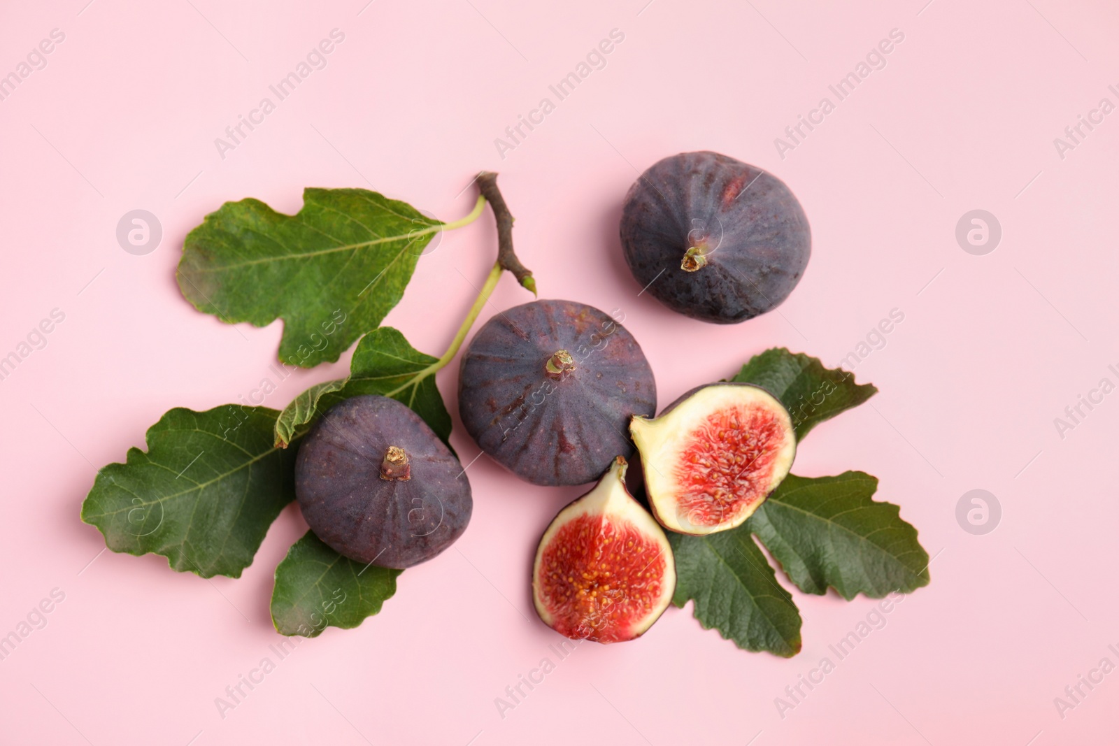 Photo of Delicious ripe figs and green leaves on pink background, flat lay