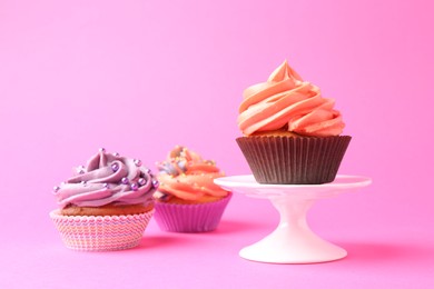 Photo of Delicious cupcakes with bright cream and sprinkles on pink background. Space for text