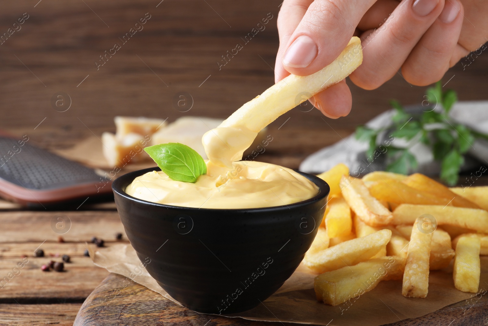 Photo of Woman dipping delicious French fries into cheese sauce at wooden table, closeup