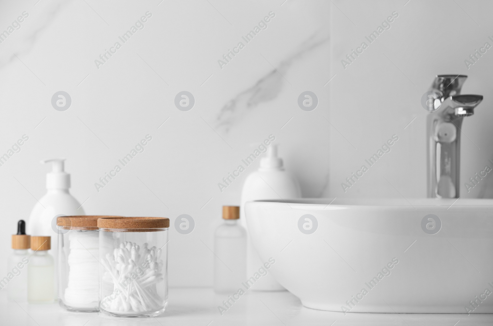 Photo of Glass jars with cotton pads and swabs near cosmetic products on white countertop in bathroom