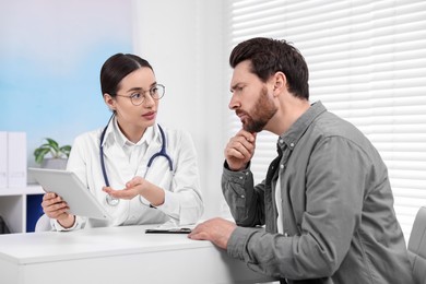 Photo of Doctor with tablet consulting patient during appointment in clinic