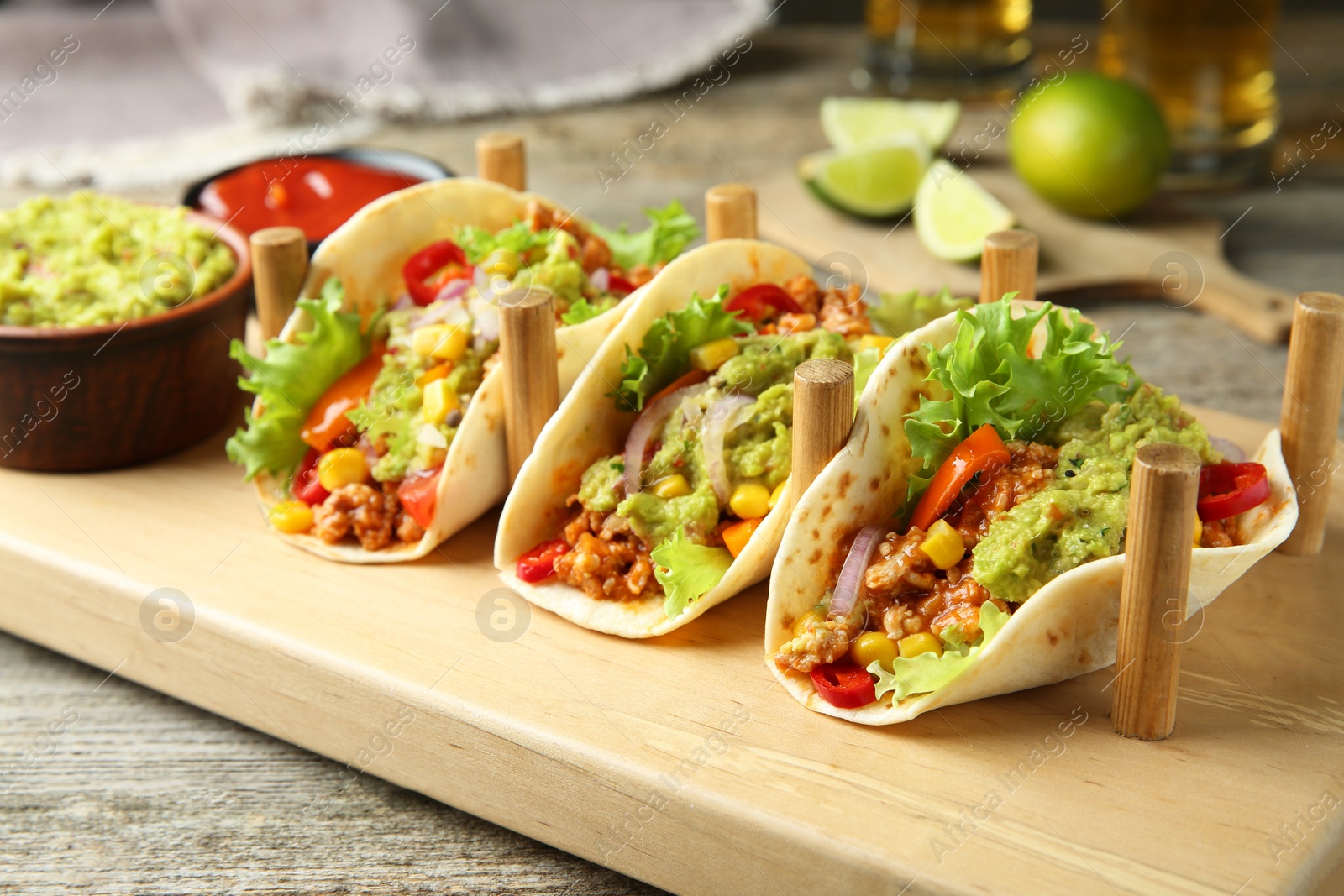 Photo of Delicious tacos with guacamole, meat and vegetables served on wooden table, closeup