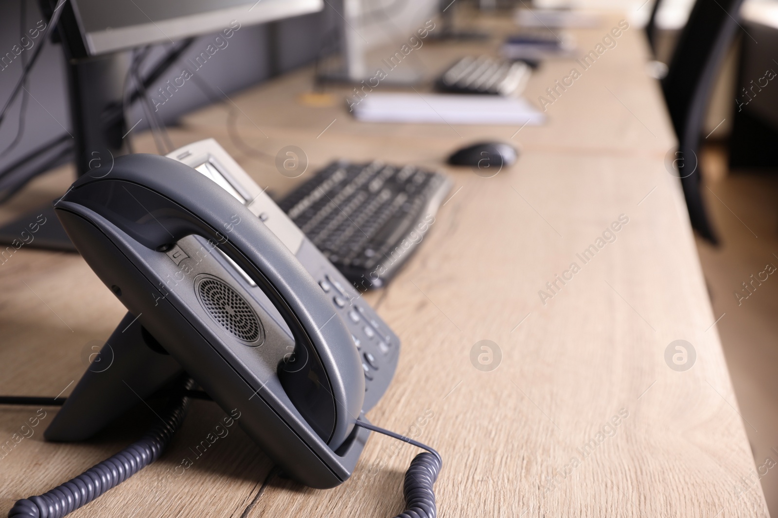 Photo of Stationary phone near modern computer on wooden desk in office. Hotline service