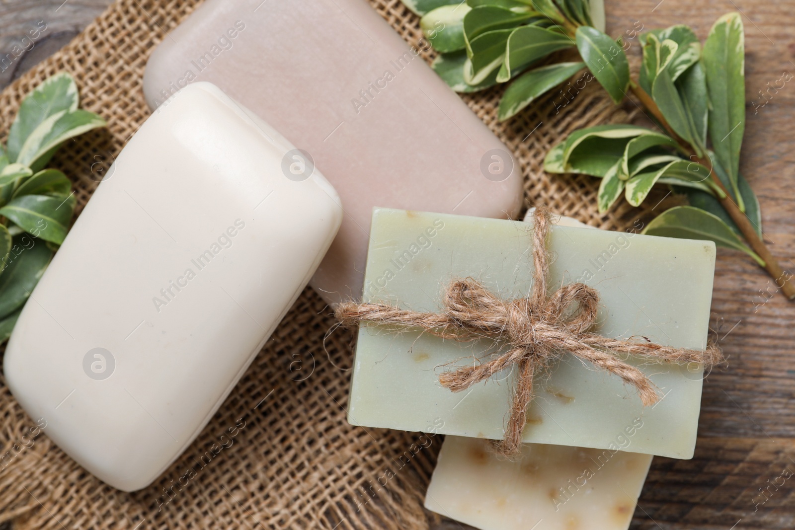 Photo of Different soap bars and green plants on wooden table, flat lay