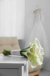 Beautiful calla lily flowers tied with ribbon on white chest of drawers indoors