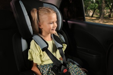 Photo of Cute little girl sitting in child safety seat inside car