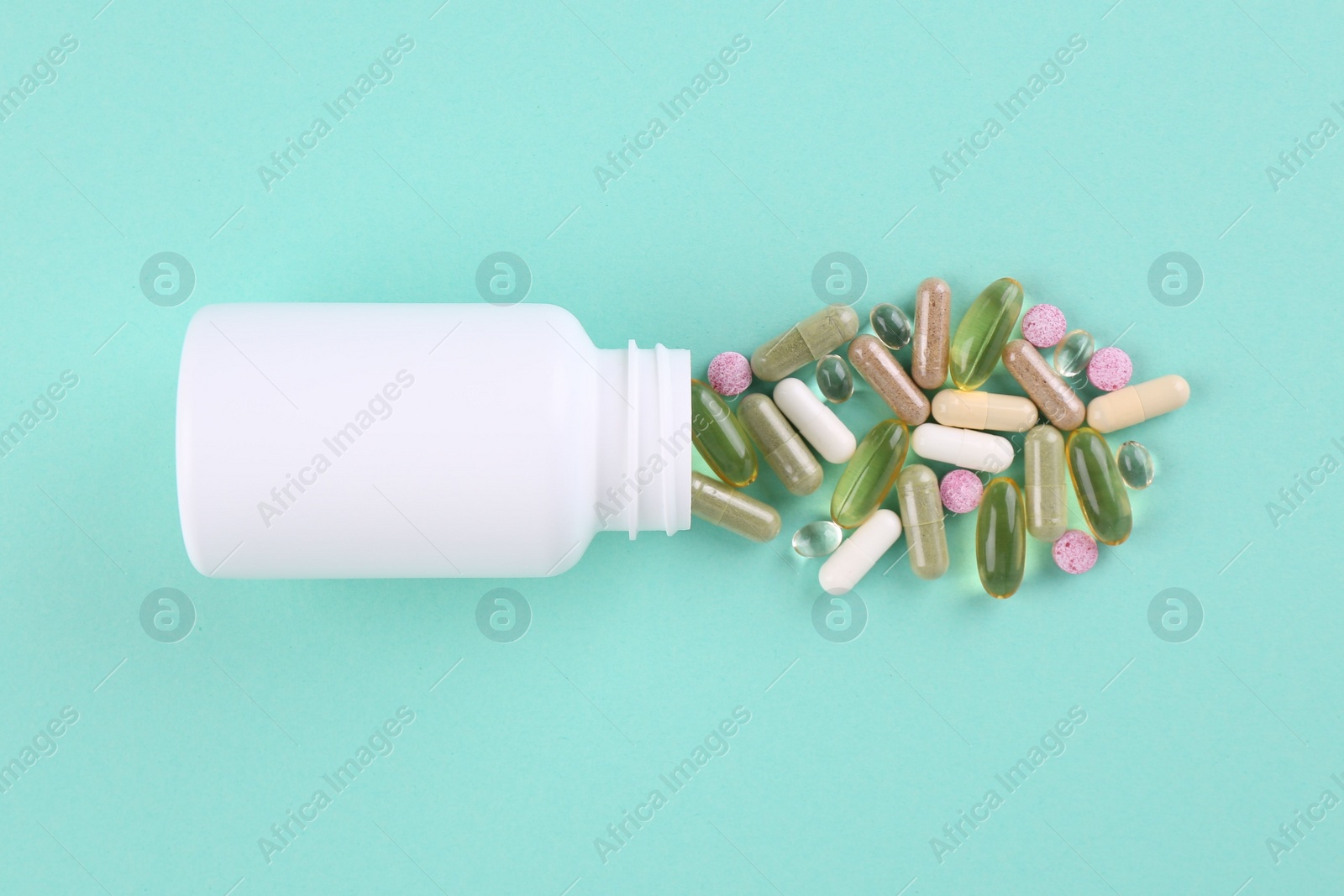 Photo of Bottle and different vitamin pills on turquoise background, top view