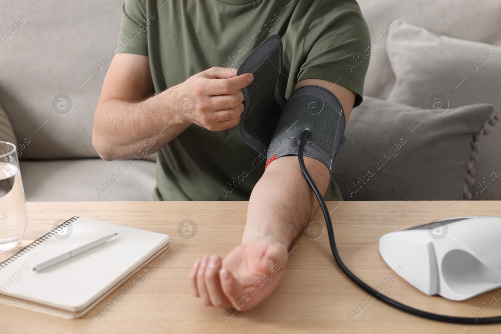 Photo of Man measuring blood pressure at wooden table in room, closeup