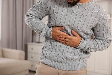Photo of Young man suffering from stomach pain indoors, closeup
