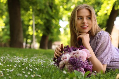 Beautiful woman with bouquet of spring flowers on green grass in park, space for text
