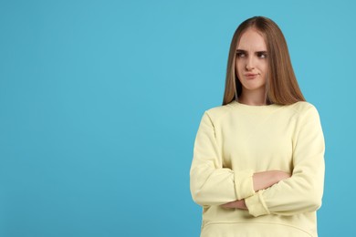 Resentful woman with crossed arms on light blue background, space for text