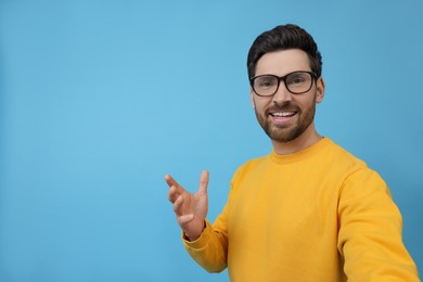 Smiling man taking selfie on light blue background, space for text