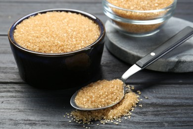 Photo of Brown sugar in bowls and spoon on black wooden table, closeup