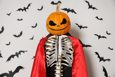Photo of Skeleton in cloak with pumpkin head and paper bats on light wall